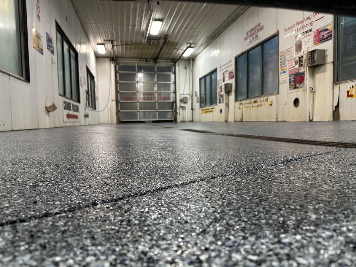 Low-angle view of an empty, well-lit car wash bay with textured flooring, closed garage door, and instruction signs on white walls.