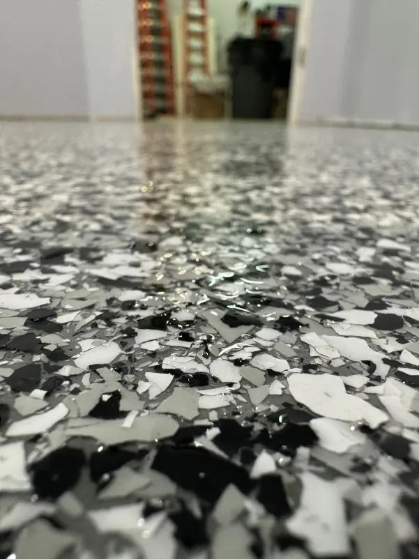Close-up of a speckled epoxy floor, leading to an open doorway. Interior shelves and a trash can are visible in the background.