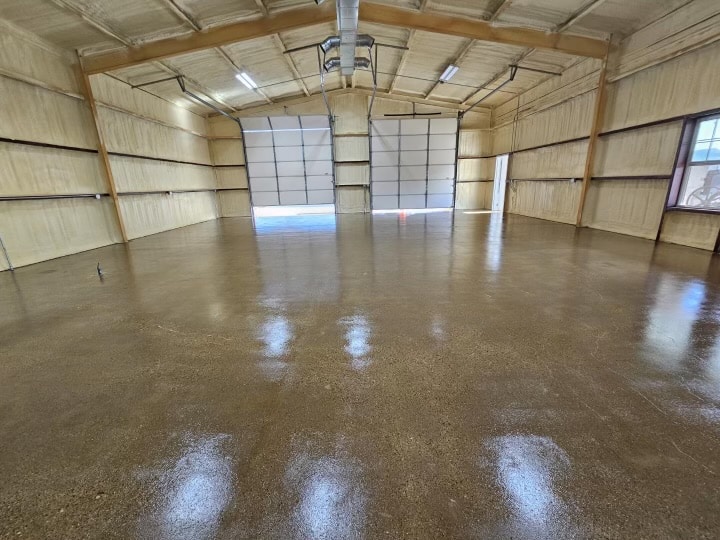 A spacious, empty warehouse interior with polished concrete floors, high ceilings, and large garage doors. Natural light streams through windows and open doorways.