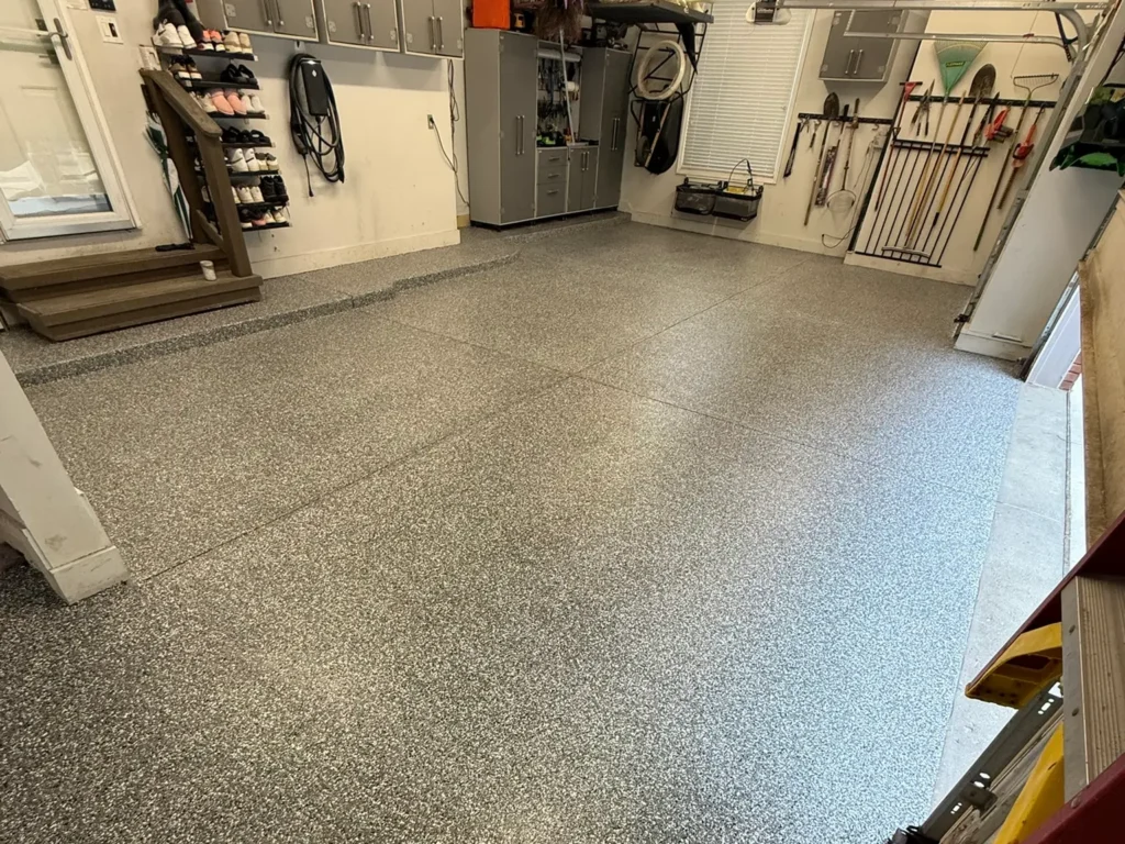 A tidy garage with speckled floor, neatly organized tools on walls, cabinets, and shoe racks, creating a well-maintained and functional storage space.