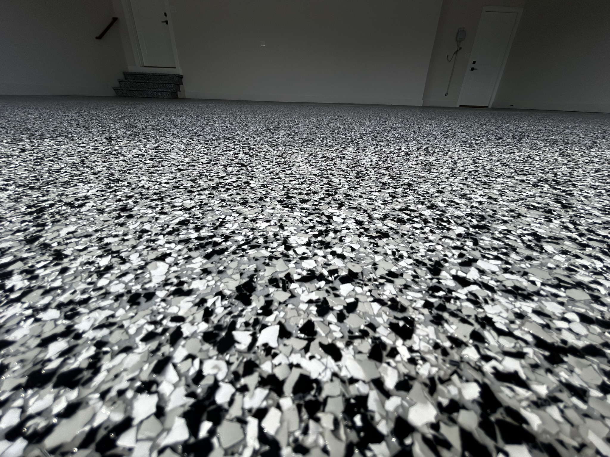 The image shows a close-up of a speckled epoxy floor, leading to stairs and doors in a sparsely decorated room.