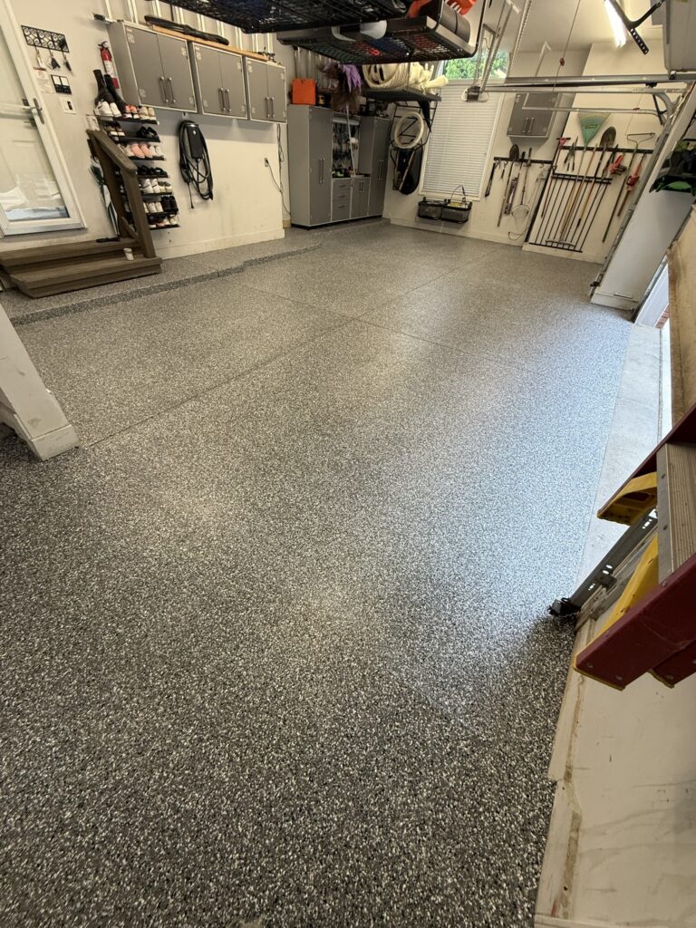 Residential garage epoxy flake flooring in gray with built-in cabinets and overhead storage
